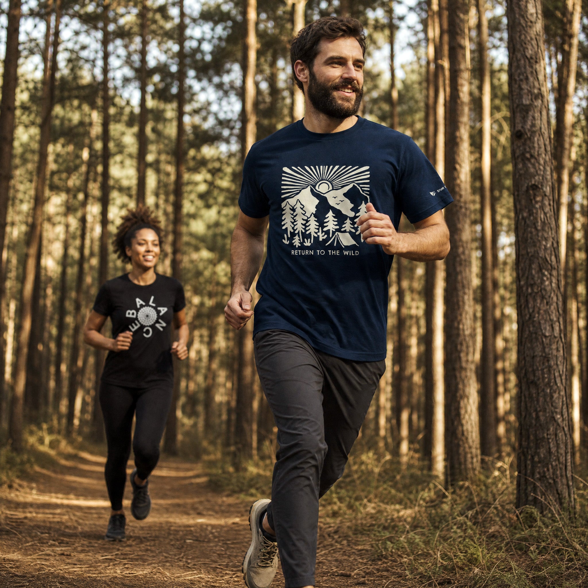 Two people running in a forest wearing matching t-shirts with nature-themed designs.