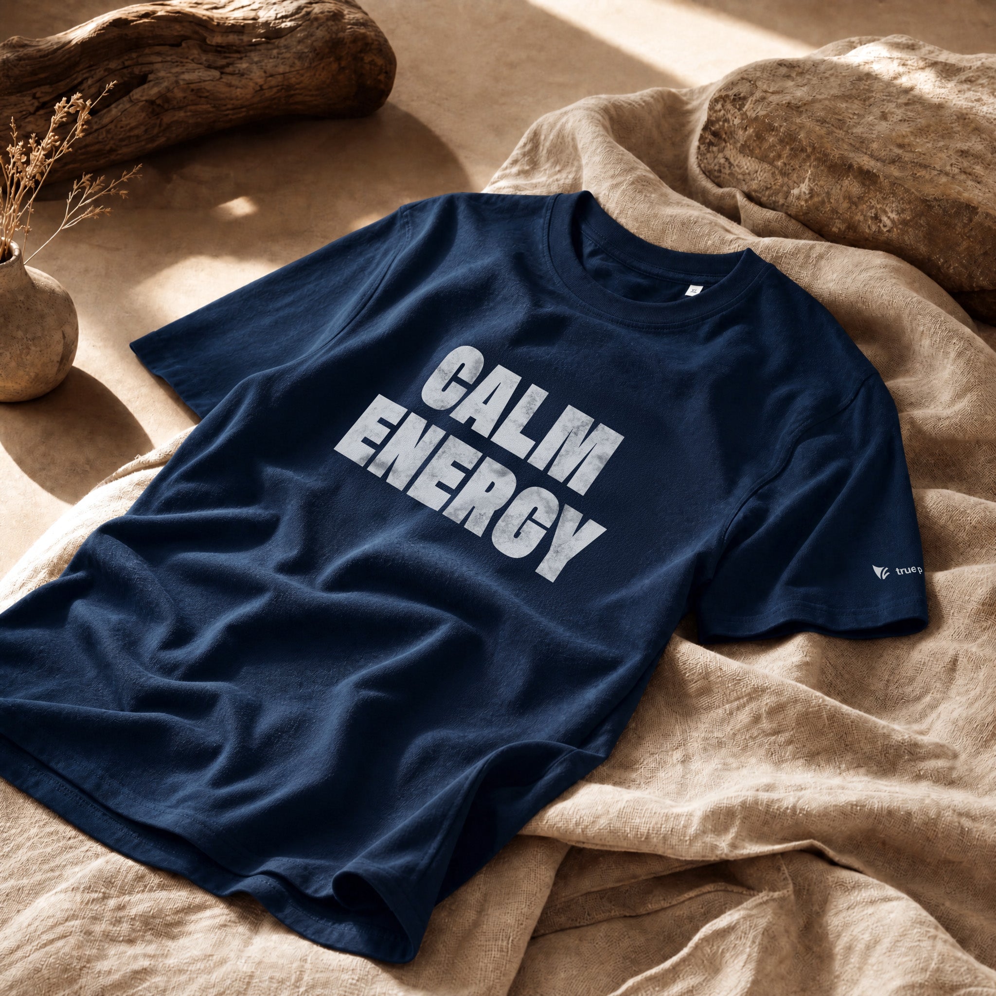 Navy blue t-shirt with 'CALM ENERGY' text on a beige surface with natural elements.