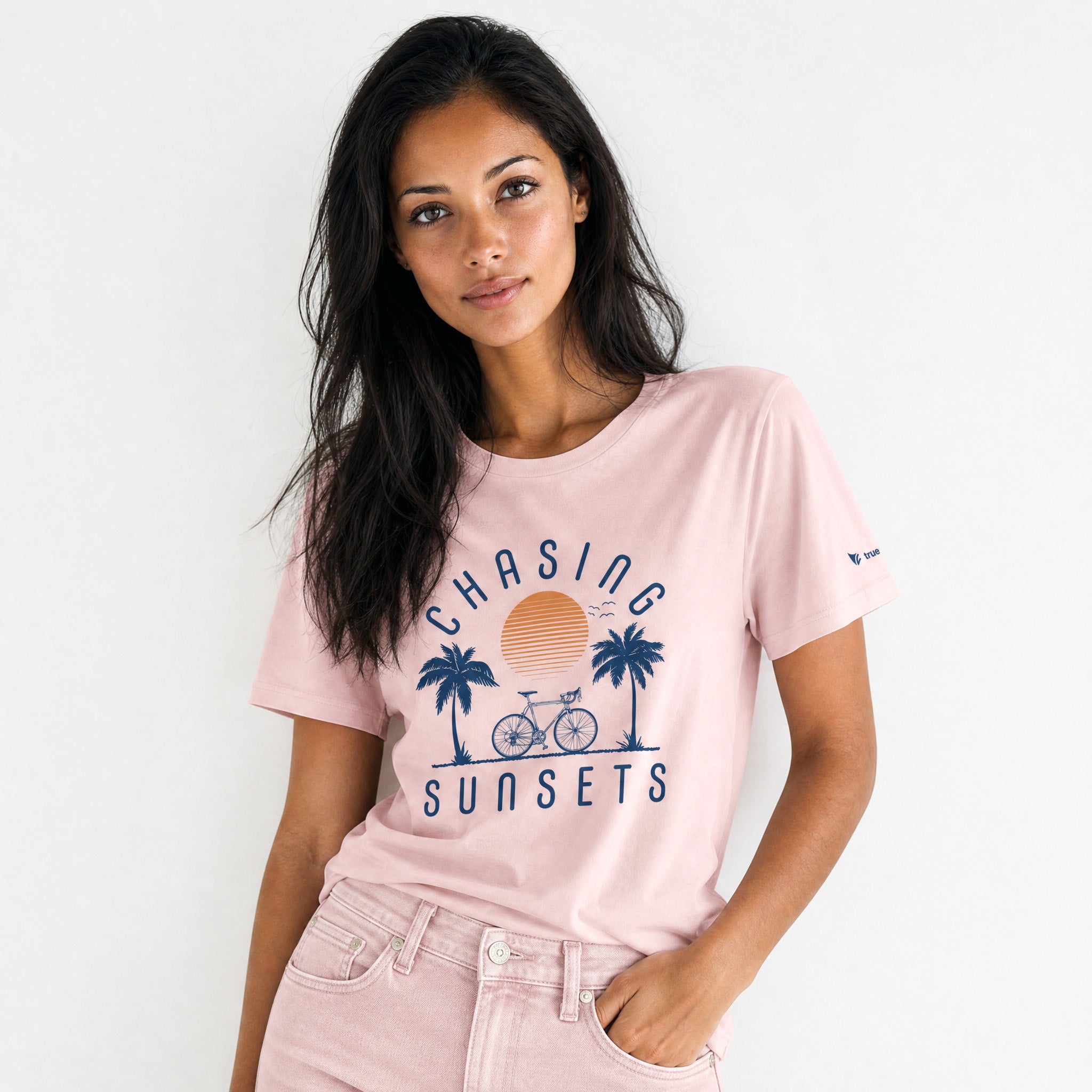 Woman wearing a pink t-shirt with 'Chasing Sunsets' graphic design on a white background